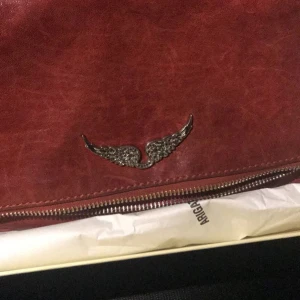 Röd zadig väska - Säljer min röda zadig väska, jättefin men i använt skick. Den har inga tydliga defekter men den är som sagt i använt skick vilken man också ser på första bilden. Även lite av silvret på kedjorna har försvunnit men inget man tänker på. 