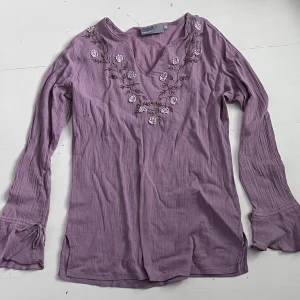 Lila blus y2k Kappahl  - Jättefin lila blus från Kappahl ca 2000-tal🌸Supergulliga blommor runt halsen och små snörningar vid ärmarna🌸I nyskick! Storlek 36 men passar även mig som är 34. 