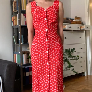 Blommig klänning  - Rödblommig vintageklänning. Har aldrig använt. Det finns möjlighet att ha skärp till, det finns öglor på sidorna i midjan - tyvärr var originalskärpet borta redan när jag köpte den. 