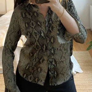 Grön ormmönstrad blus - Ormmönstrad grön blus från Neo Noir. Knappar framtill