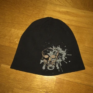 Black ” Skull ” Beanie. - Svart mössa med tryck på. Använd men fortfarande i användbart skick. Små trådar som sticker upp på ett ställe. Möts bara upp i Stockholm. Postar ej.