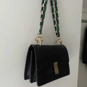 Handväska  - En stor och rymlig handväska från Gina tricot. Jag har bytt ut bandet då jag inte gillade originalet så den som är på just nu kommer frå NAKD. Svart väska med fina gulddetaljer och ett grönt band som ger färg på en outfit. 