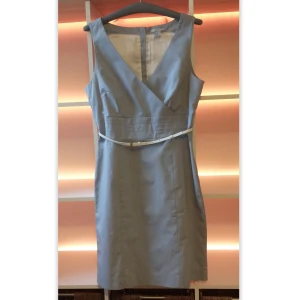 Klänning, H&M, M - Grå klänning från H&M med vit bälte och dragkedja i storlek 42, men liten i storleken. Storlek passar för M. Från armhålan till armhålan 49cm. Midja 40cmx2, längd 96cm. Nyskick.