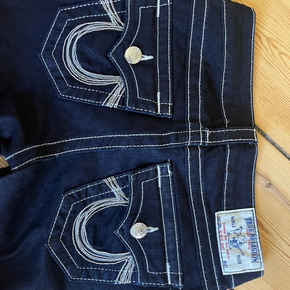 Äkta true religions jeans, väldigt mörk blåa med silvriga nästan vita sömmar.  Fickorna har silver och stenar på fickorna. Jag är 163 cm! Aldrig använda, köpt för 1800kr i london. . Jeans & Byxor.