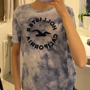 Holister t-shirt  - Holister tröja med blått vitt mönster. Svart tryck fram. I storlek L men skulle säga att den mer liknar en M. Bra kvalitet, använd ett fåtal gånger👍🏼