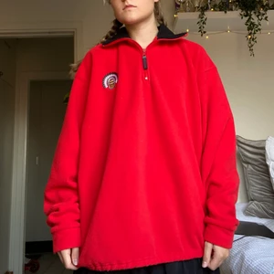 Röd fleece med tryck - En röd fleece tröja med svart krage, liten dragkedja och ett indian tryck på bröstet. 100% polyester. Tvättas i 40°C. ✨