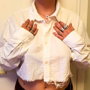 VIT SKJORTA I AVKLIPPTA DESIGN - vit skjorta i avklippta design med trådar hängandes från nedre delen av tyget 