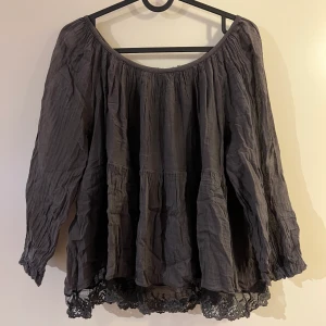Blus - En mörkgrå blus med spets nedtill. Korta ärmar. Vet inte vart den kommer ifrån. Storlek M