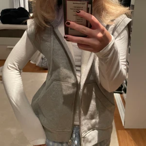 Hoodie väst i grå med zip - Ziphoodie utan ärmar i grått från otherstories, köpt för ca 2 år sedan, nypris 700kr, nyskick använd en gång, säljer eftersom den inte riktigt är min stil. Skriv vid intresse eller frågor❤️