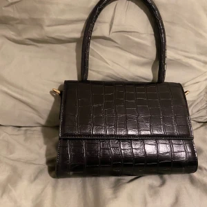 NAKD-väska - Väskan är ca 23x17 cm stor och har ett styvt handtag. Den är köpt för ca 2 år sedan men knappt använd. Det finns en liten slitning som syns på bild men den är knappt märkbar;)