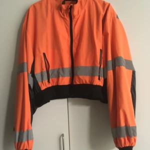 Orange jacka från Poster Girl - En jättefin jacka från Poster Girl. Den har reflexer både fram och bak. Passar bra som en höstjacka då den är lite fodrad på insidan. Det är storlek S/M men ganska oversized och croppad i modellen. 