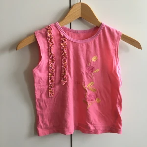 Rosa magtröja - Min systers rosa linne/magtröja, med blommigt mönster och detaljer. Lappen är avklippt men liten i storleken, dock stretchig! Den enda defekten är att nedre sömmen lossnat lite, se bild 3. Längd från kragen 36 cm, bredd mellan armhålorna 34 cm.
