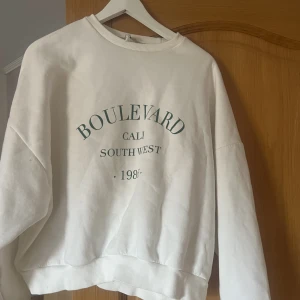 Sweatshirt  - Säljer denna vita sweatshirt med grönt tryck från Nelly. Använd fåtal gånger, inga defekter. 