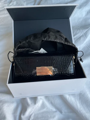 Ideal of sweden väska  - Säljer en helt ny svart axelremsväska från ideal of sweden i modellen ”black rocco bag”. Nypris är 899kr. Den är helt ny, aldrig använd, förplackning, låda och påse finns kvar och medkommer. ❤️Axelrems bandet medkommer och har nitar i form av prickar på.