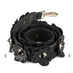 Väskrem med nitar  - Säljer denna väskrem/axelrem med svarta blommor och nitar på från Gabriella by p, 4 cm brett och ca 1m lång. 