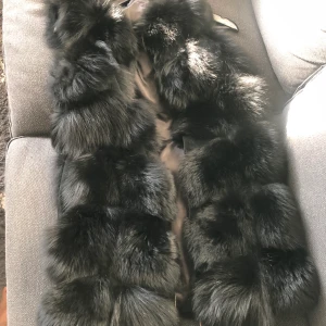 faux päls väst - Pälsvästen är i fluffig fin rävpäls som går i parallella rader. Mellan raderna är de kortklippt mjuk kaninpäls som fyller mellanrummen så den känns extra lyxig och fluffig. Västen är fodrad vilket gör den användbar utomhus i kallt väder med en varm tröja.