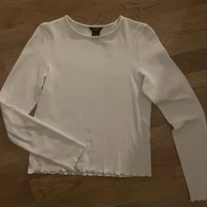 Vit långärmad topp - En vit långärmad topp med vågiga kanter ifrån Lindex. Ribbat material. Passar både storlek xs och s. Väldigt bra skick.