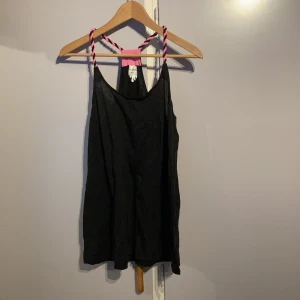 Linne från Monki - Ett lite längre linne från Monki med rosa/svart flätade band. Är i storlek x-small. Materialet är delvis bomull.