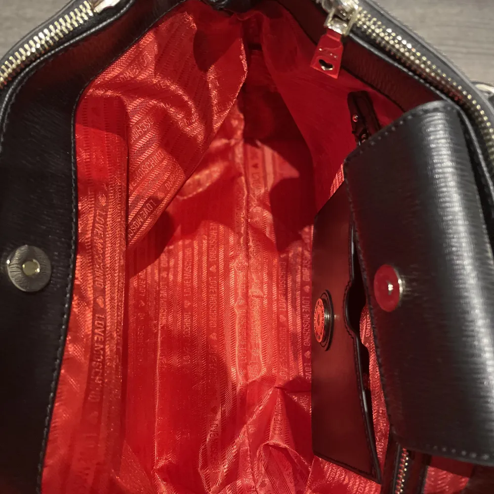 Love Moschino-väska som knappt är använd överhuvudtaget, inga repor i varken lädret eller fodret. Rött fodral på insidan med två små och två stora fickor. Går att sätta på axelband (medföljer) Ca Bredd 41cm x Höjd 23cm x Djup 23 cm.. Väskor.