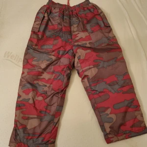 Täckbyxor barn  - Rosa camouflage täckbyxor I st 120 till barn. Ej används, inget slitage. Snöra i midja för att spänna. En ficka på varje sida.  Kan skicka fler bilder vid förfrågan. 
