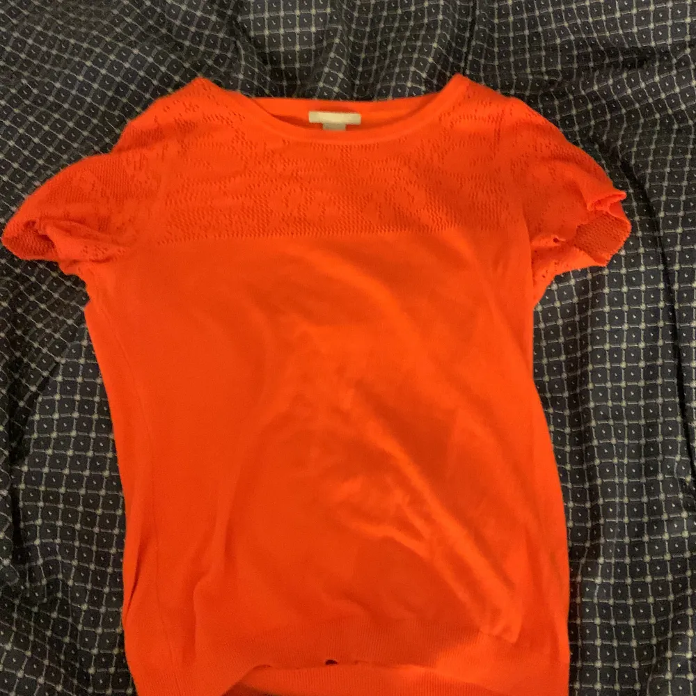 En orange stickad tröja med fina detaljer längst upp. Stickat.