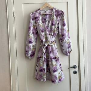 Lila omlottklänning med blommigt mönster. Går att använda som lättare jacka om man inte knyter klänningen. Storlek 42! 
