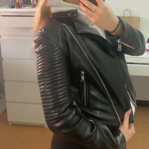 Svart Skinnjacka  - En svart skinnjacka (ej äkta skinn) från Zara i storlek S/36. Knappt använts och är lika bra som ny. Funkar super för vår vädret som närmar sig. Alla fickor är äkta, bra material, superfin på. 