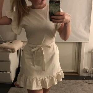 Vit klänning  - Super fin vit klänning i lite tjockare material med fina volanger nertill och vid armarna, och fickor på båda sidorna säljer jag då jag aldrig använt den, bandet runt magen går att ta bort, super skön en varm sommardag kan jag tänka mig 