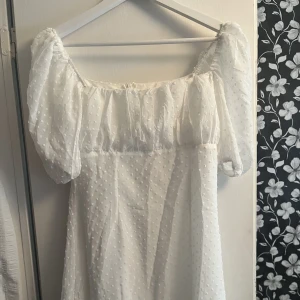 Vit klänning - Fin vit klänning med puffärmar och längd till mitten av låret. Dragkedja på ryggen. Passar perfekt till studenten eller skolavslutning.  Storlek 38. Aldrig använd. 