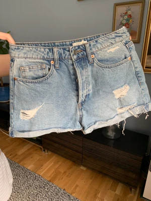 Jeansshorts - Jeansshorts med slitningar från H&M, strlk 36. På mig som har mellan strlk 36-38 sitter de högmidjat och tajt. Allmänt fint skick, men köpta på stadsmissionen.