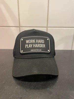 John hatter keps - Sparsamt andvänd. Rubber cap. Inga knappar har lossnat på baksidan. Den har inte tappat formen heller.