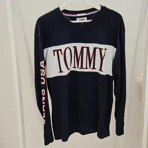 Det är en tun tröja med märket tommy jeans  På högra armen står det jeans USA  Mörkblå 