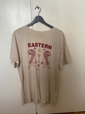 Tshirt - Fin beige tshirt från gina tricot med mörkrött tryck. Använd ett fåtal gånger! Storlek L