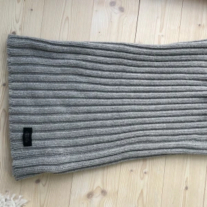 Stickad tubhalsduk - Skön halsduk från Adrian Hammond i grå färg. Halsduken är varm och sticks inte.