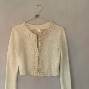 Kort handgjord kofta  - Benvit handgjord kofta från hm nyårskollektion 2006 . Knäpps med hyskor( några är lite lösa  Med pärlor 