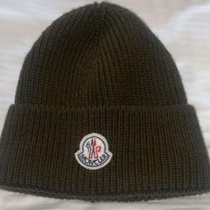 En helt ny moncler mössa i modellen Wool Beanie och är i en mörk olive grön färg. Den är helt ny och är i ett perfekt skick. Ingen prislapp på!