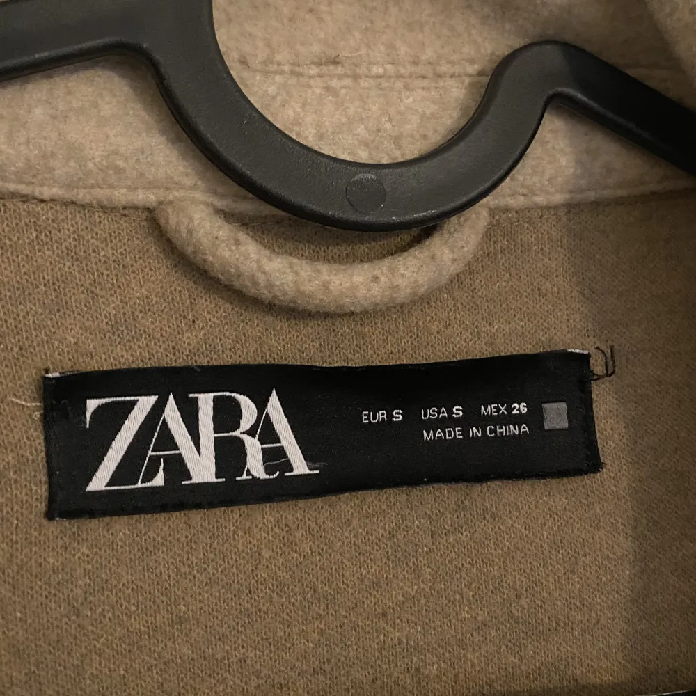 Brun/beige kappa i strl S från Zara, använd flertals gånger och är i ok skick. Kappan har svarta knappar med vit/bruna detaljer på.  Kontakta för fler frågor/bilder :) köparen står för frakten. Jackor.