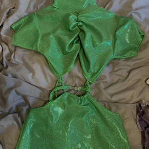 "Disco" klänning - Lime grön glansig klänning från Roxanna The Label:  Rygglös, turtleneck, utskuren klänning med dragsko Tillverkad av limegrön holografisk stretchlycra Med "Disco" bokstäver Justerbar passform, knytband både upptill och på sidan 