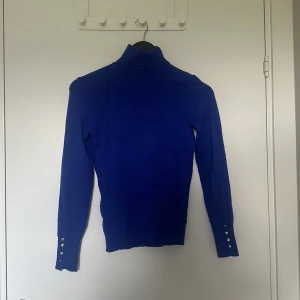 Blå polo tröja med guldknappar - Säljer denna polo som jag fått, men som inte passar min storlek. Har guldknappar som detaljer längst handlederna och är snygg på. 
