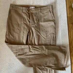 Beige kostymbyxor i jeansmaterial - Snygga och coola beiga kostymbyxor i jeansmaterial, i low waist modell från ASOS. Passar till mycket och går att både klä upp och klä ner. Dessa är köpta i storlek 40 för att få en mer baggy look. 