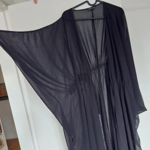 Kimono - Svart mesh-liknande, supertunt material. Knyt i midjan. Mycket lång (släpar i marken för 167 cm) och fladdrar superdramatiskt i vinden! Perfekt för både stranden och utekvällen. Passar i princip S till XXL+