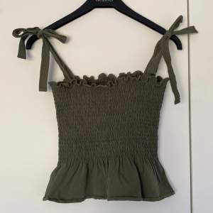 Ett croppat linne med smock och knytband i khakigrön bomullsblandning. Supersmidig och skön att ha på stranden över en bikini eller till en fin kjol🥥🥥