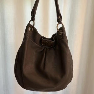 Marc jacobs väska - Väska från Marc jacobs. Vintage och har några skrapsår fram och uppe längst kanten. Med lite vård kan den bli som ny! Fin på insidan, inget trasigt där. Perfekt storlek att ha på axeln och får plats med det mesta.