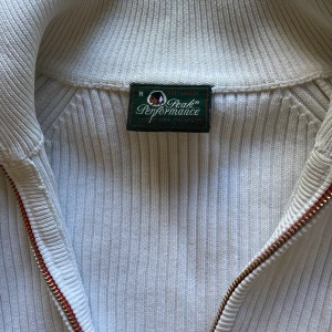 Kofta från peak performance - Vit ribbad kofta från Peak Performance med en krage och zip dragkedja framtill som man kan styra vringningen. 