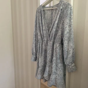 Blåblommig klänning  - Vit och ljusblå klänning med volanger i nederkant. Strl 38 från Nelly. Mycket sparsamt använd, dock har lite tråd gått upp i ena ärmen men det är inget som syns. 