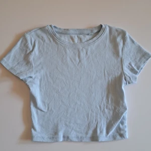 Ljusblå Ribbad T-shirt - Kroppad ribbad T-shirt. Bara använd ett fåtal gånger. Kontakta gärna vid fler frågor eller bilder på T-shirten!💕
