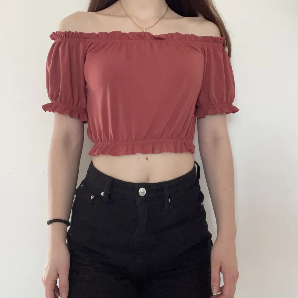 Stretchig crop top med fina detaljer från Gina Tricot i stl XS. Rosa/korallaktig färg i lite skimrigt material. Offshoulder. Fint skick då den knappt är använd. Material: 95% polyester, 5% elastan. Djur- och rökfritt hem.. Toppar.