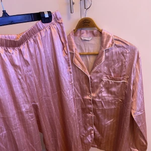 Lounge underwear pyjamas - En rosa satinpyamas från lounge underwear. Skjortan är i L och byxorna i XL. Små i storleken passar M/L. Byxorna är låg/mid waist. 
