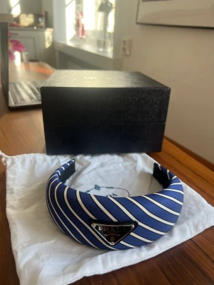 Diadem från Prada - Blå, vit och svart randigt diadem från Prada. Använt ett fåtal gånger, som nytt. Kvitto, dustbag och kartong finns.   Nypris: 4450kr
