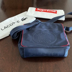 Supreme x Lacoste Messenger Bag  - Använd vid ett fåtal tillfällen, ända lilla defekten är på bild 3 (färg som lostnat). Enl bild 1 ingår supreme plastpåse och Lacoste tygpåse. Totalt 4 separata fack. Färg: Navy. Kom gärna med frågor i pm!:) Kram!❤️☮️